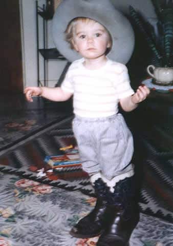Polly as a kid wearing her dad's cowboy hat and boots.