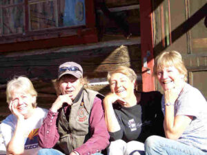Polly and three sisters in front of an old log cabin, each with her chin on her right hand and elbows on knees.